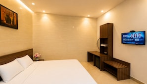A hotel room with a large bed, a TV mounted on the wall, a wooden cabinet, and a small desk.