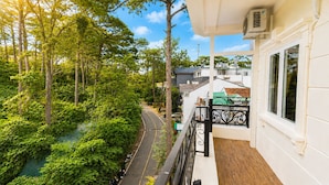 A balcony with a view of a road and greenery, a white building with a window, and an air conditioning unit. - Lien's 2 Hotel Da Lat (Xuan Huong - Da Lat)