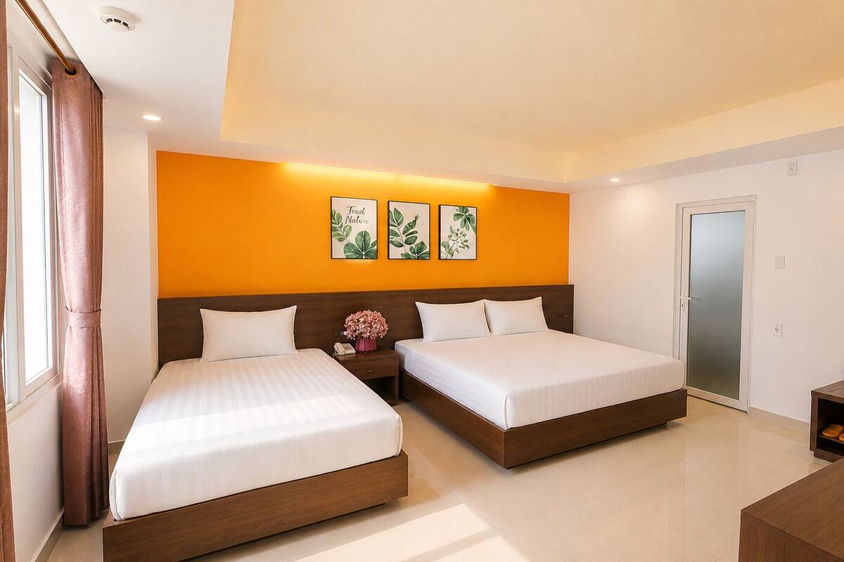 A hotel room with two beds, a nightstand with a phone and flowers, a wooden bench, and a sliding door.