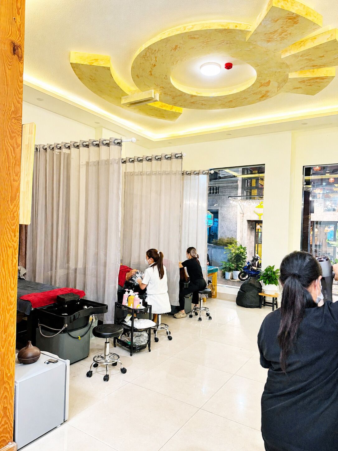 Un salón con un diseño moderno en el techo, un ventanal grande y una barra con herramientas de peluquería.
