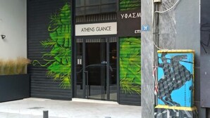 A building entrance with a sign reading "ATHENS GLANCE" and a mural of green leaves on the wall.