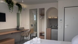 A modern hotel room with a bed, a desk, a chair, a bathroom, and a kitchenette.