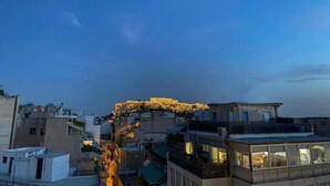 A cityscape at dusk with a prominent ancient structure on a hill, surrounded by modern buildings.