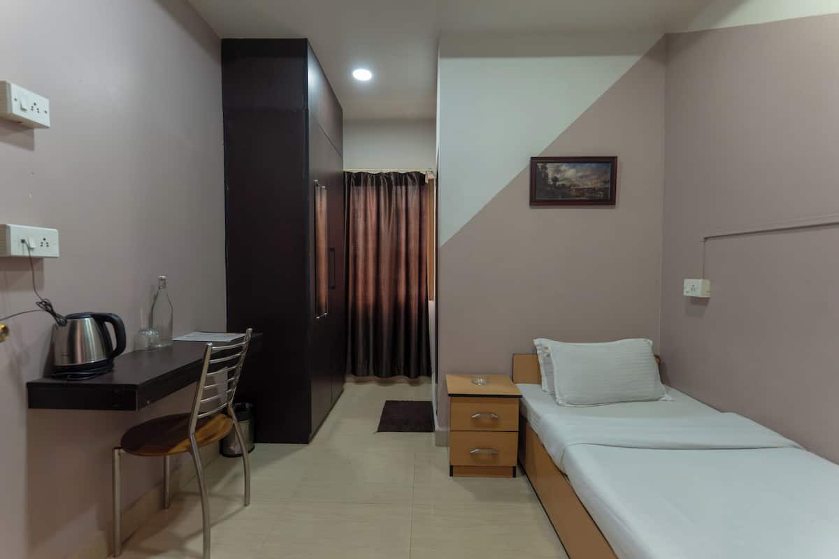 Habitació petita i compacta amb un llit, escriptori amb cadira, taula petita i un armari.