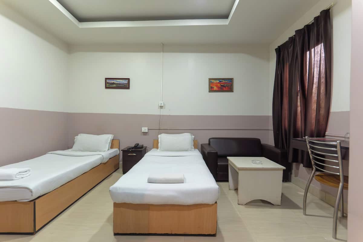 Habitació d'hotel amb dos llits individuals, un escriptori, una cadira, una taula petita i un sofà.