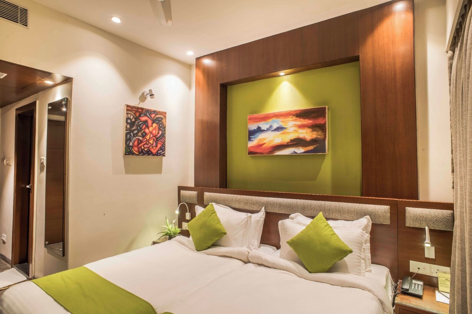 A hotel room with a large bed, green pillows, a painting on the wall, and a bedside telephone.