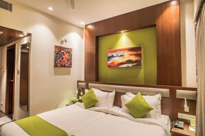 A hotel room with a large bed, green pillows, a painting on the wall, and a bedside telephone. - Club Central Hotel (Bolpur)