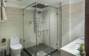 A modern bathroom with a glass-enclosed shower, a toilet, and a sink with a plant. - Club Central Hotel (Bolpur)