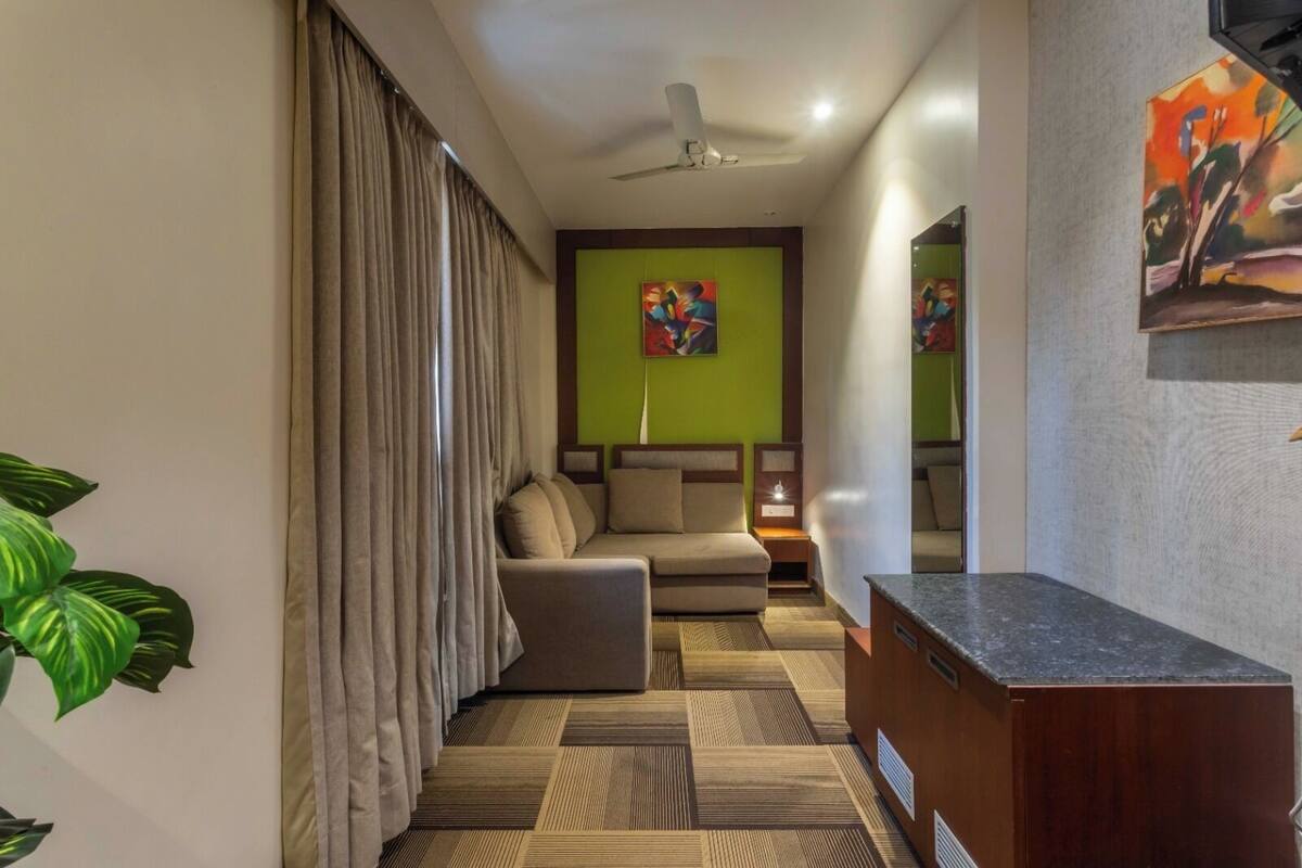Una habitación de hotel moderna con sofá, una mesita, ventilador de techo y un cuadro en la pared.