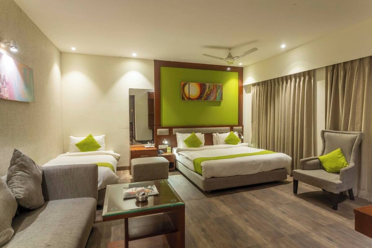 Habitación de hotel con dos camas individuales, un sofá, una silla, una mesita y un ventilador de techo.
