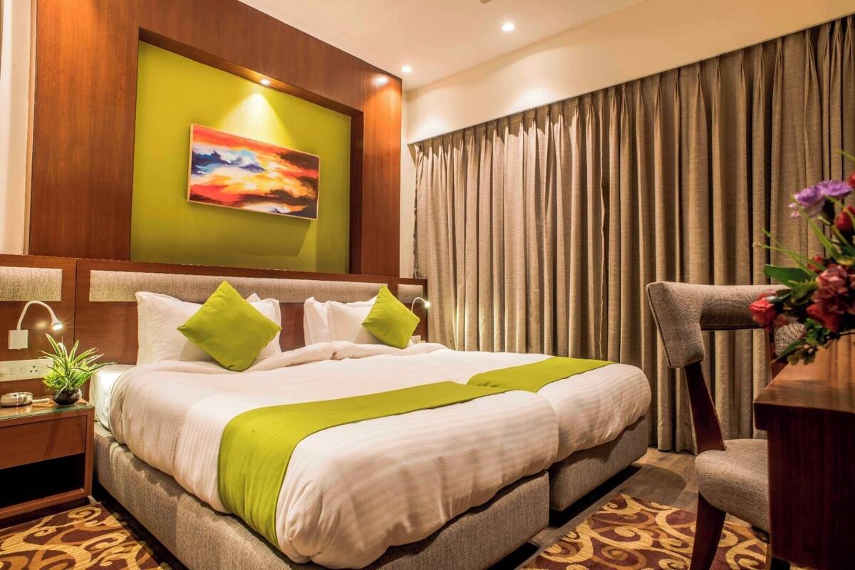 Una habitación de hotel con una cama grande, almohadas verdes, un cuadro en la pared y una cortina.