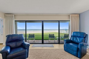 A room with two leather armchairs facing a large sliding glass door leading to a balcony with a view of the beach.