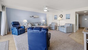 Una sala de estar con un sofá azul, un sillón azul, un sillón a rayas, un ventilador de techo y una alfombra.