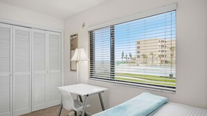 Una habitación con una cama, un escritorio, una silla, una ventana con persianas y una puerta con contraventanas.
