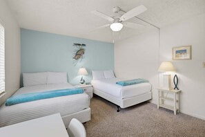 A bedroom with two beds, a ceiling fan, a nightstand with a lamp, and a framed picture on the wall.