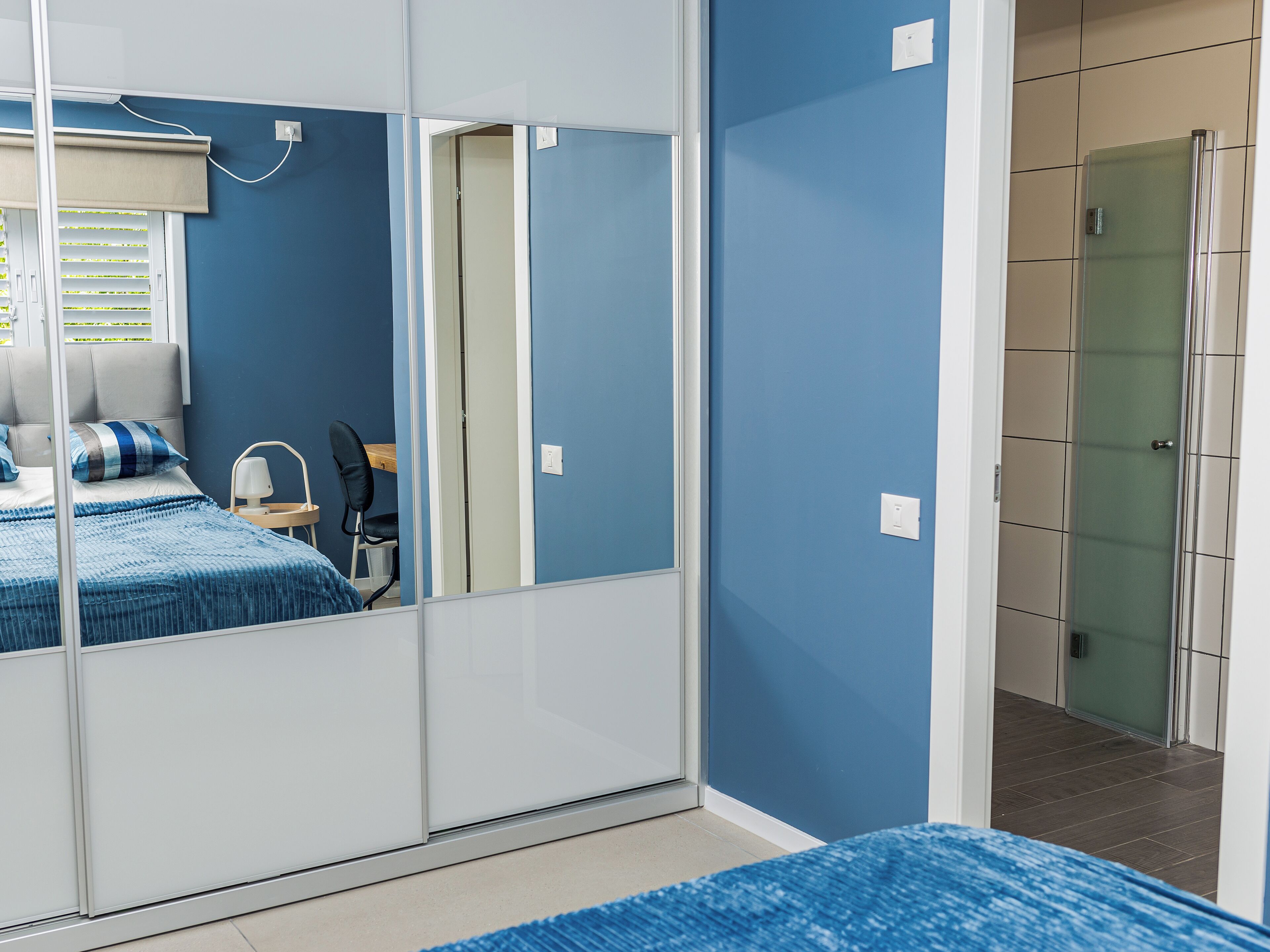 Quarto com cama, uma cadeira, escrivaninha e guarda-roupa.