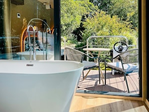 Une salle de bain moderne dotée d’une grande baignoire, d’une douche à l’italienne avec des parois en verre et offrant une vue sur un jardin luxuriant grâce à une grande fenêtre.