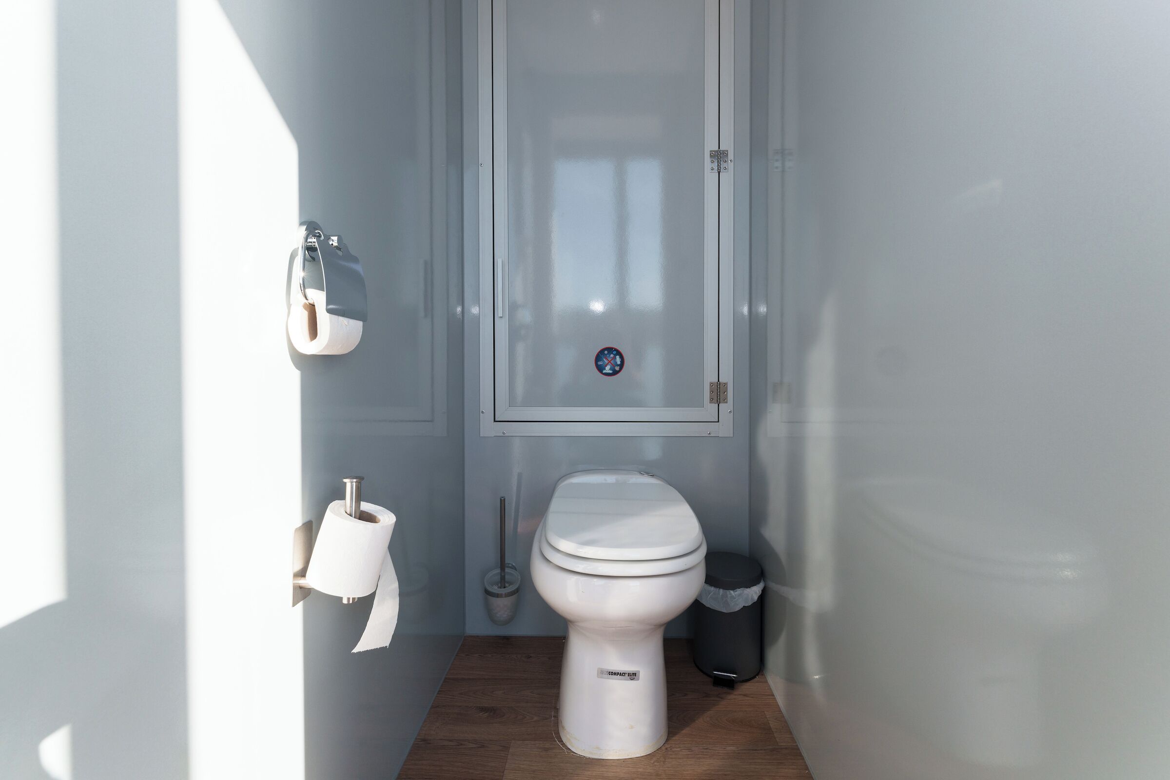 A small, modern bathroom with a toilet, a trash bin, and a toilet paper holder.