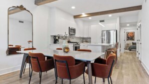 Una cocina moderna con armarios blancos, una isla central y un comedor con mesa blanca y sillas naranjas.