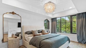 Un dormitorio con una cama grande, un espejo, una araña y vistas a árboles por la ventana.