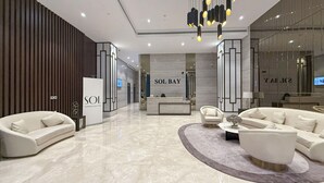 A modern hotel lobby with a reception desk, seating area, and a large mirror reflecting the interior.