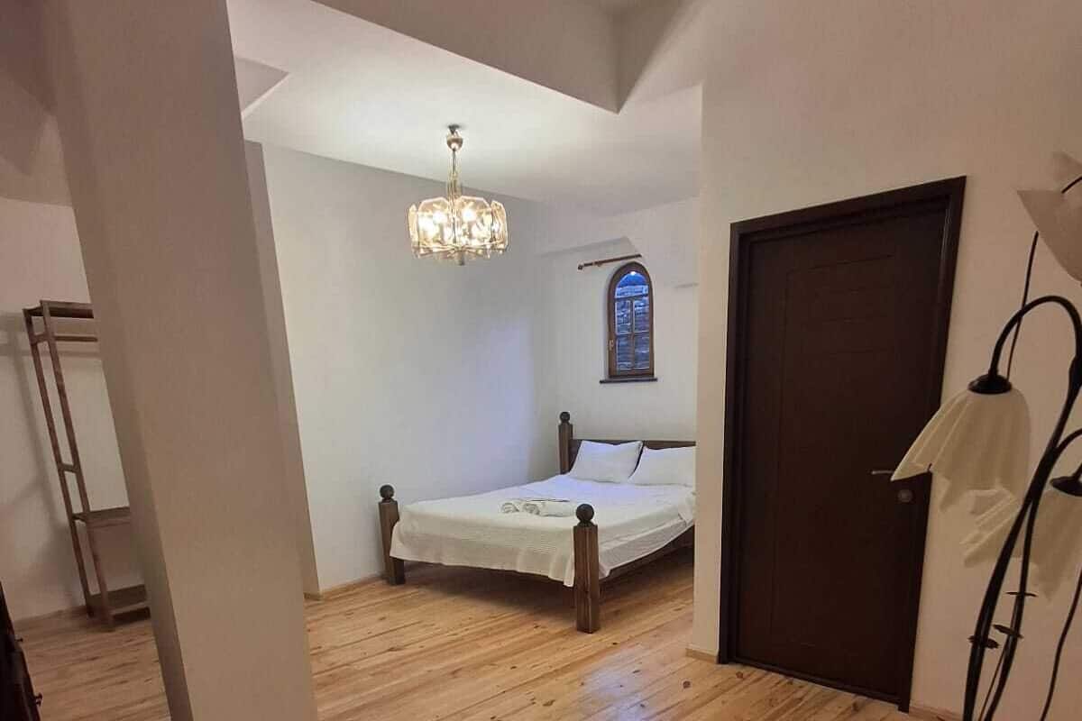 Ein Schlafzimmer mit Holzboden, einem Bett mit weißer Bettwäsche, einer Kristallleuchtre, einem Fenster und einer Tür.