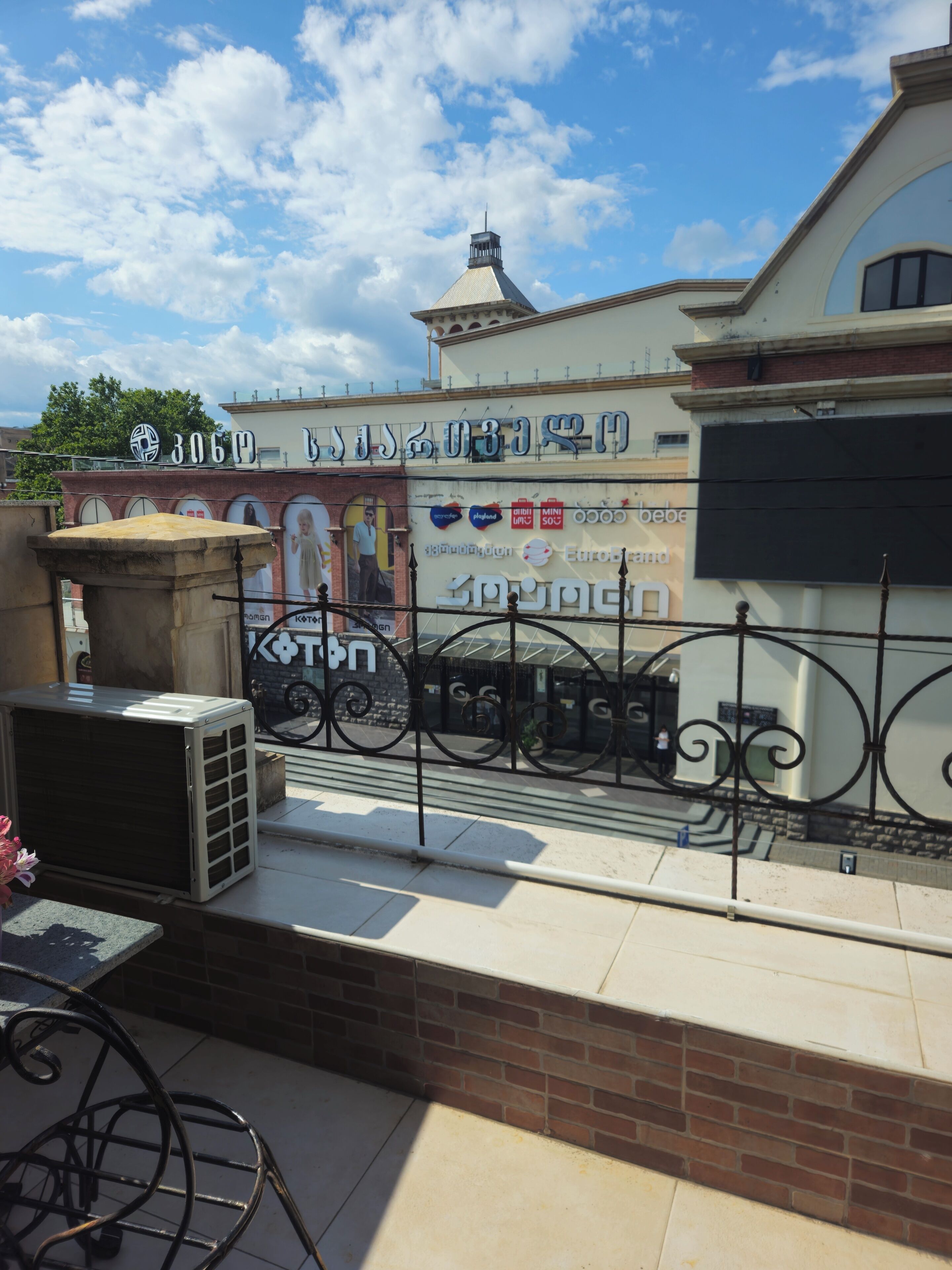 A building with a large sign in a foreign language, a brick wall, and a metal fence.