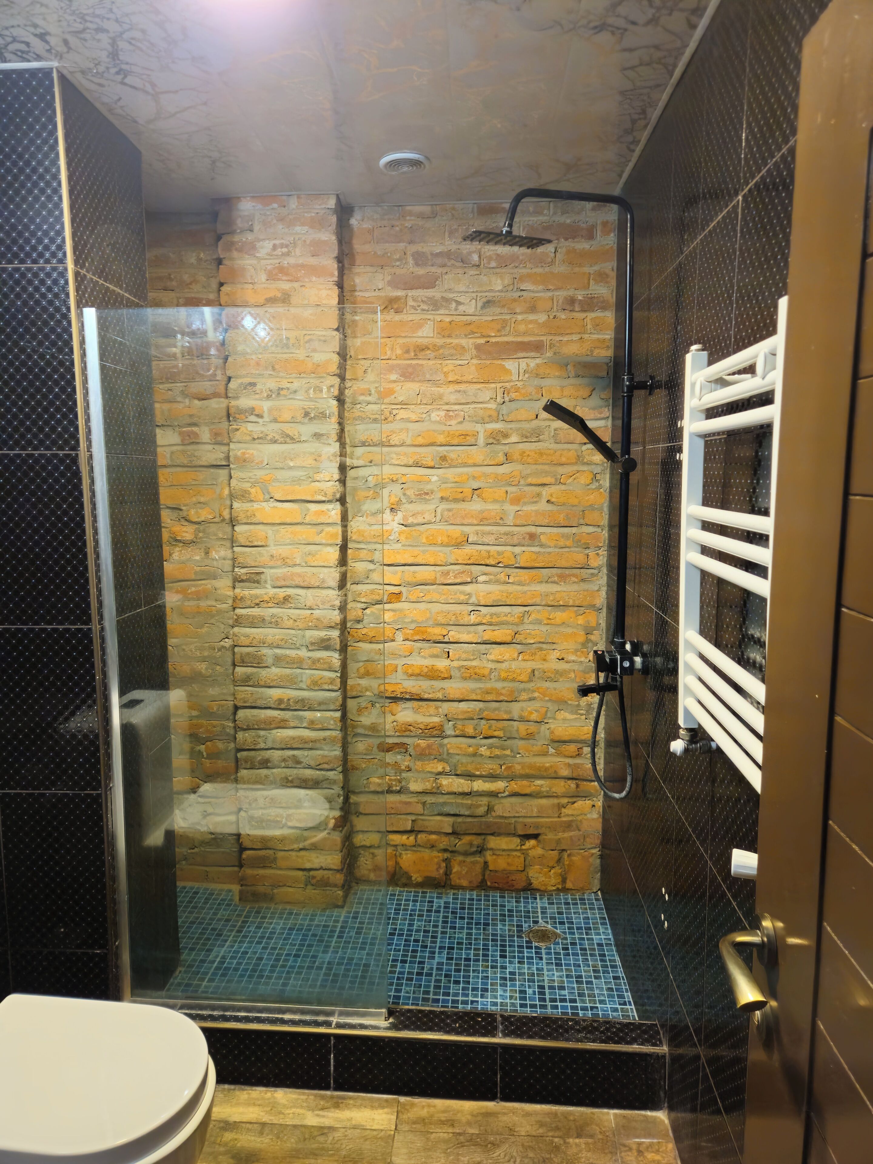 A shower area with a glass door, a brick wall, and a tiled floor.