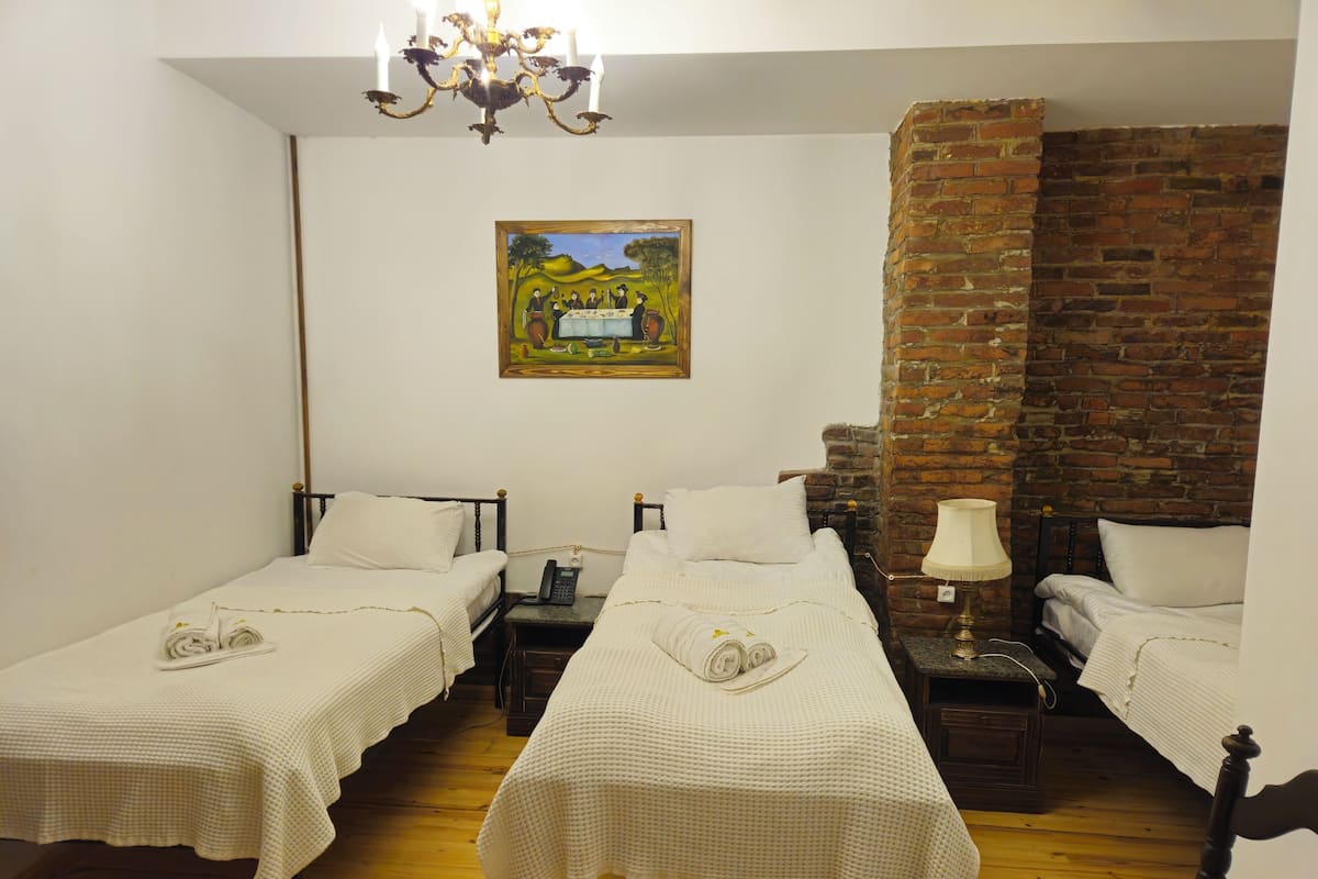 Ein Zimmer mit zwei Einzelbetten, Holzboden, Backsteinwand, einem Gemälde an der Wand und einer Chandelier.