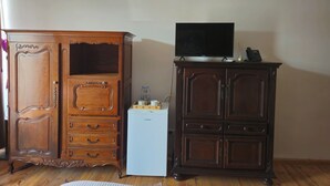 Quarto com um armário de madeira, uma geladeira branca e uma televisão sobre outro armário.