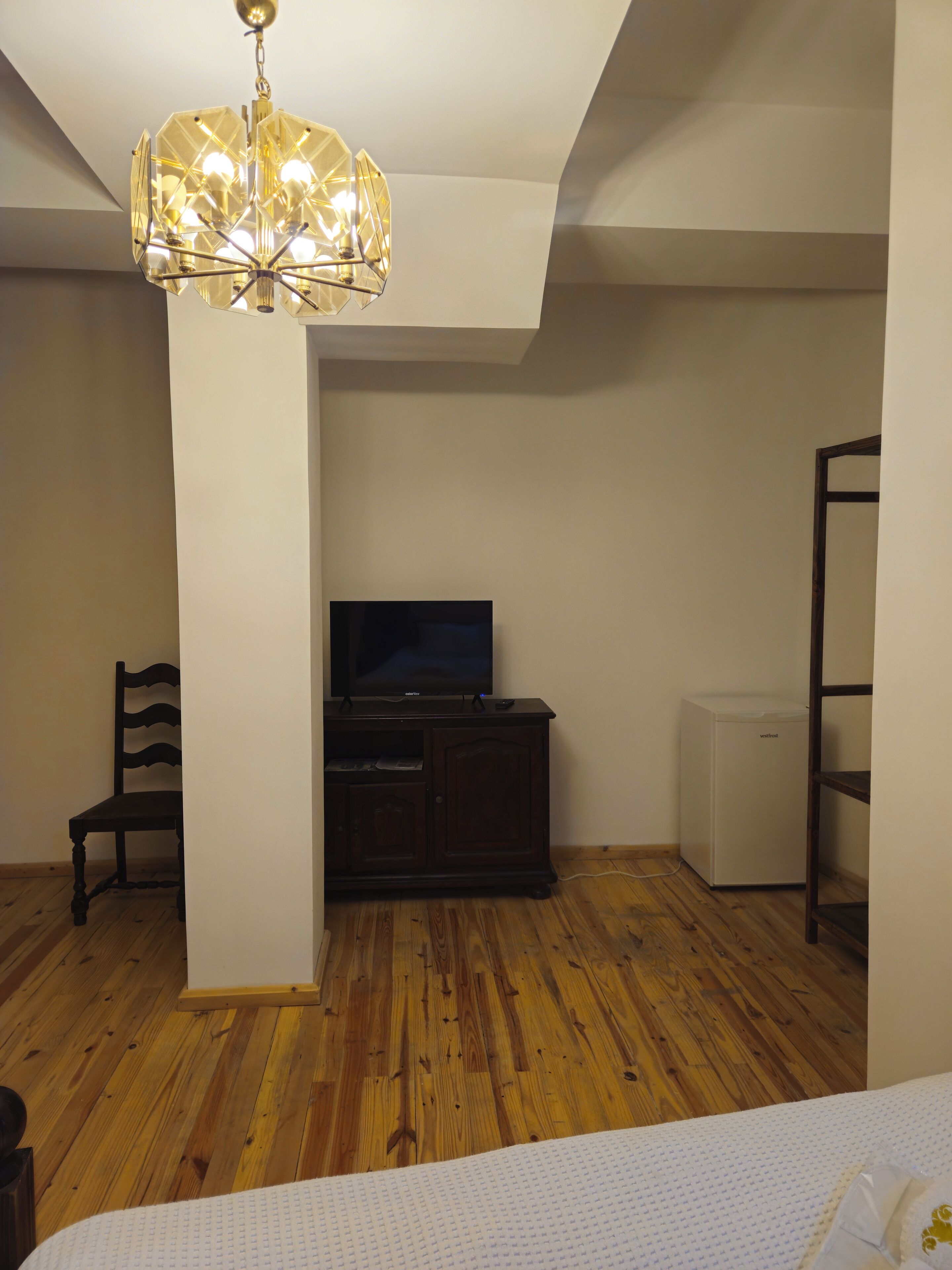 Ein Zimmer mit Holzboden, einem Fernsehgerät auf einem dunklen Holzschrank, einem weißen Kühlschrank und einem Holzstuhl.