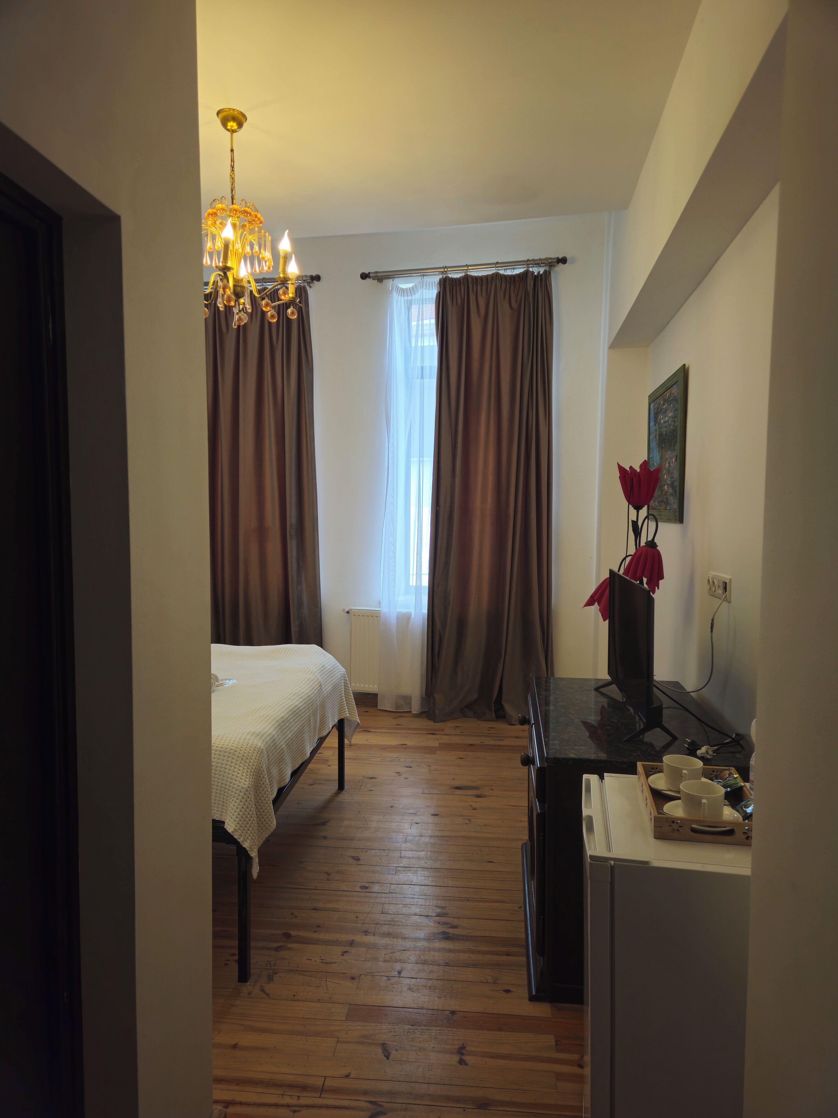 A bedroom with a bed, a desk with a computer, a radiator, and a window with curtains.
