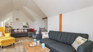 A modern living room with a grey sofa, a yellow armchair, and a wooden coffee table with pastries. - Coastguard Lookout (Weymouth)