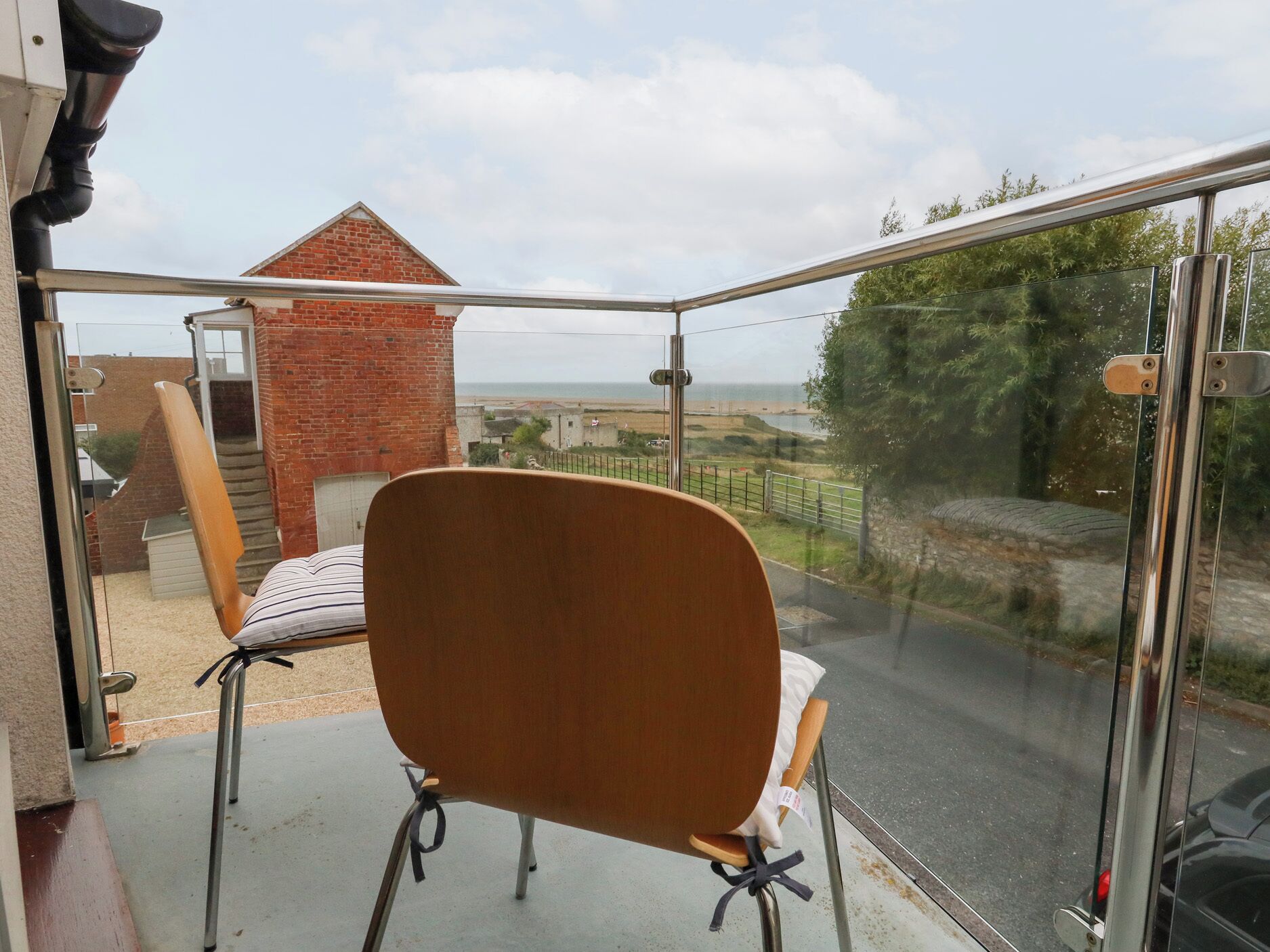 Un balcone con una sedia e un tavolo di legno, affacciato su un edificio in mattoni e sulla costa.