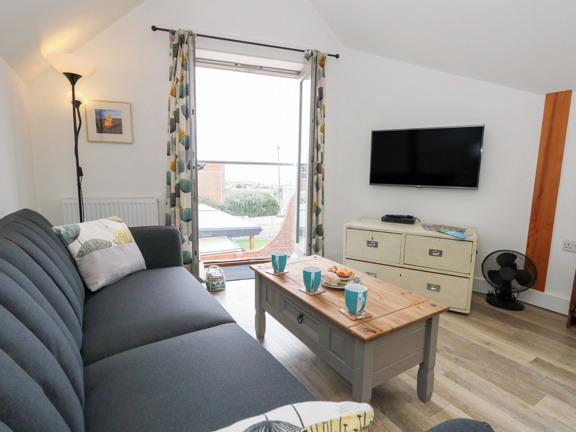 A modern living room with a sofa, a wooden coffee table, a television, and a dresser.