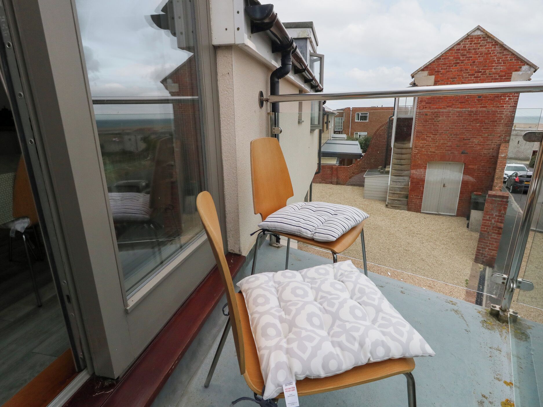 A balcony with a chair and a cushion, a sliding glass door, and a view of a brick building and a car.