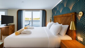 Une chambre d’hôtel avec un grand lit, un téléviseur posé sur un bureau en bois et une vue sur une étendue d’eau par la fenêtre.