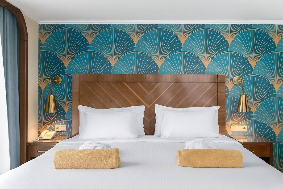A hotel room with a large bed, two bedside tables, a wooden headboard, and a patterned wallpaper.