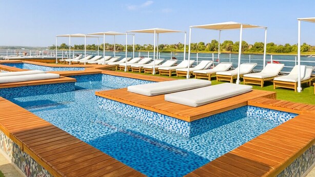 Un espace piscine doté de nombreuses chaises longues et de parasols, entouré d’une terrasse en bois et offrant une vue dégagée sur l’eau.