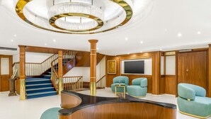 Un vaste salon doté d’une table basse en bois aux lignes courbes, de fauteuils turquoise, d’un grand téléviseur et d’un escalier avec des rampes en bois.