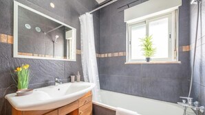 Et moderne badeværelse med en stor vask, spejl og badekar. Der er et vindue med en plante i vindueskarmen.