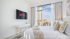 Ein luxuriöses Hotelzimmer mit einem großen Bett, einem Flachbildfernseher, der Netflix zeigt, Blick auf die Stadt und einem weißen Konsolentisch.