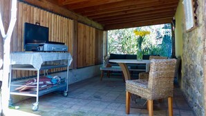 Patio esterno con barbecue, tavolo e sedie, e una poltrona in vimini.