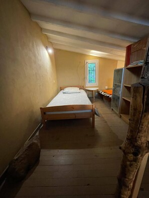 A narrow room with a single bed, a small table, and a window with a view of trees. - Le Gite du Moulin A haven of peace in the heart of the Cévennes (Aumessas)