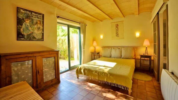 Una camera da letto con un letto, un armadietto in legno, un quadro appeso al muro e una finestra con tende.