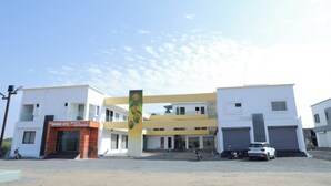 A modern building with a Mango Bite restaurant on the ground floor, a central pillar with fruit designs, and a parking area with vehicles. - Mango Bite Hotel & Restaurant (Mandvi)