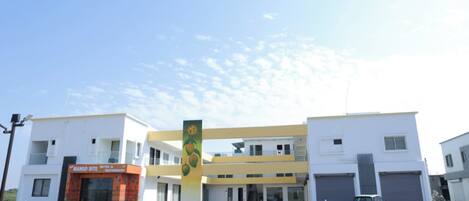 A modern building with a Mango Bite restaurant on the ground floor, a central pillar with fruit designs, and a parking area with vehicles.