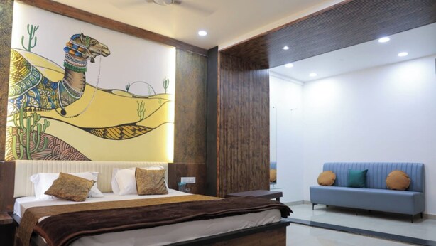 A modern bedroom with a large bed, a blue sofa, and a camel-themed mural on the wall. - Mango Bite Hotel & Restaurant (Mandvi)