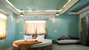A bedroom with a round bed, a smaller bed, a ceiling fan, and a wardrobe. - Mango Bite Hotel & Restaurant (Mandvi)