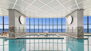 An indoor swimming pool with a clear view of the ocean through large windows, surrounded by marble walls and a tiled ceiling. - 『CASSA OCEAN』Skyline Oceanfront 2BR in Surfers "M" (Surfers Paradise)
